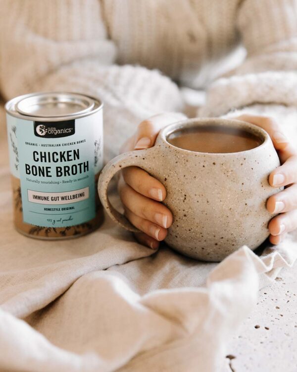 Woman snuggled up with a cup of Nutra Organics Chicken Bone Broth with product canister