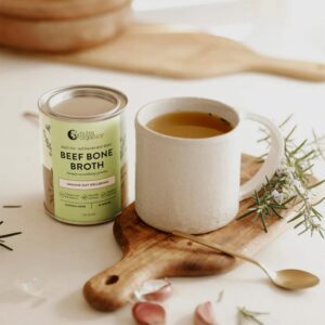 A stylized image of cup of hot Nutra Organics Beef Bone Broth in Garden Herb flavour alongside a 125g container of the product
