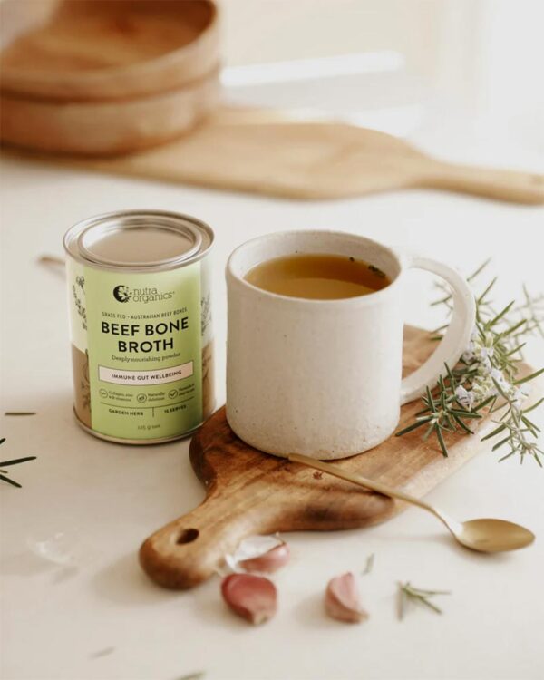 A stylized image of cup of hot Nutra Organics Beef Bone Broth in Garden Herb flavour alongside a 125g container of the product